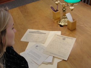Jessica examines documents containing George Sr.'s promotion to Corporal and his Honorable Discharge forms
